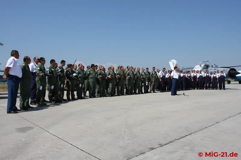Against the backdrop of the MiGs and the assembled pilots and technicians, the base commander concludes the …